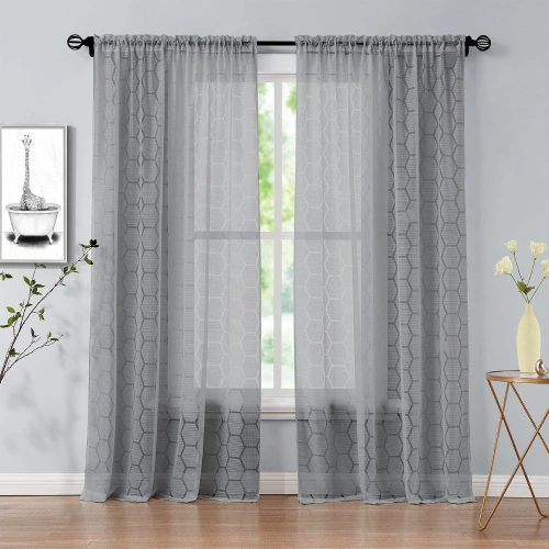 Grey lace sheer curtains with a geometric honeycomb pattern hanging over a window in a bedroom