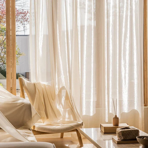 Sheer curtains hang over a large window, allowing soft natural light to fill a modern living room