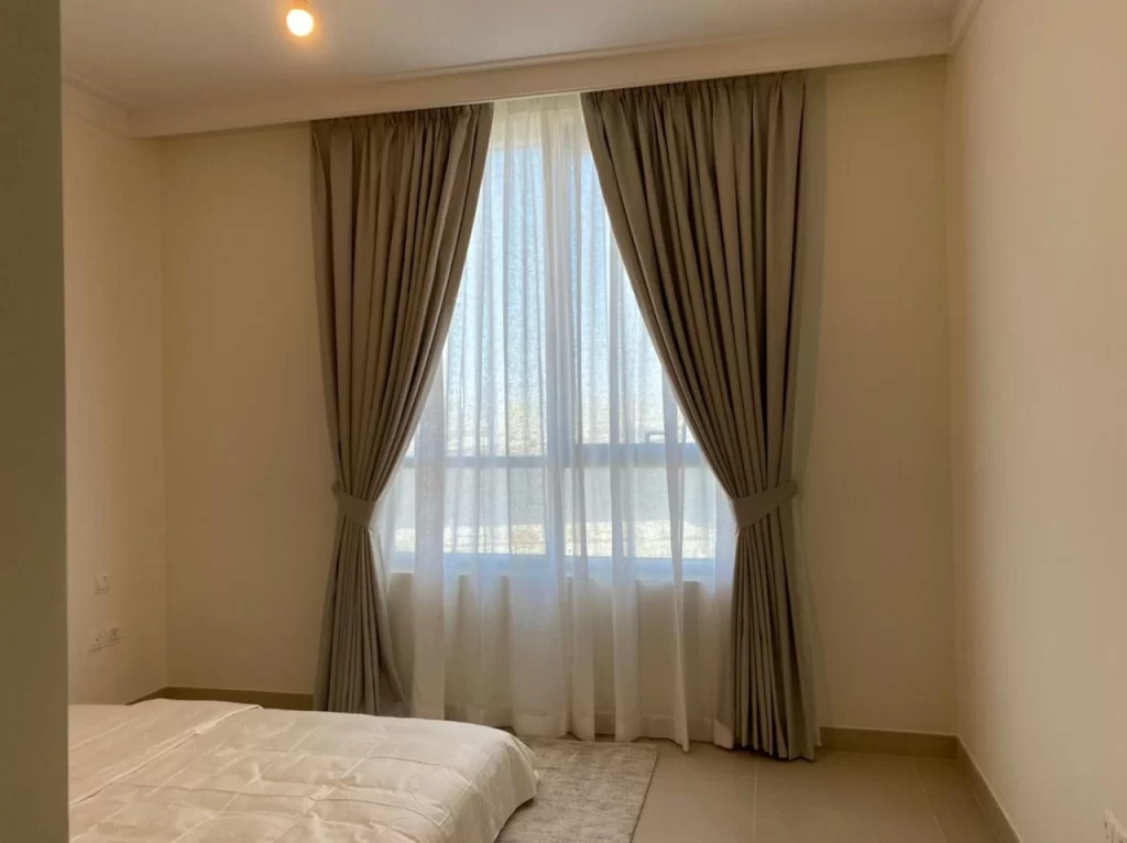 Bedroom with a window featuring beige blackout curtains and sheer white drapes