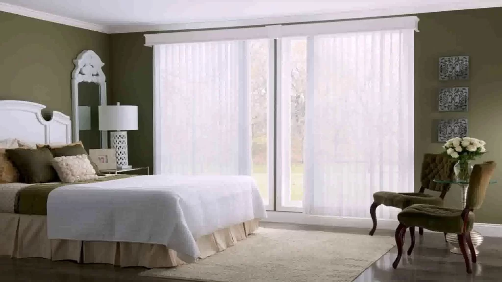 Bedroom with vertical white blinds covering large windows, an olive green wall, and a white bed