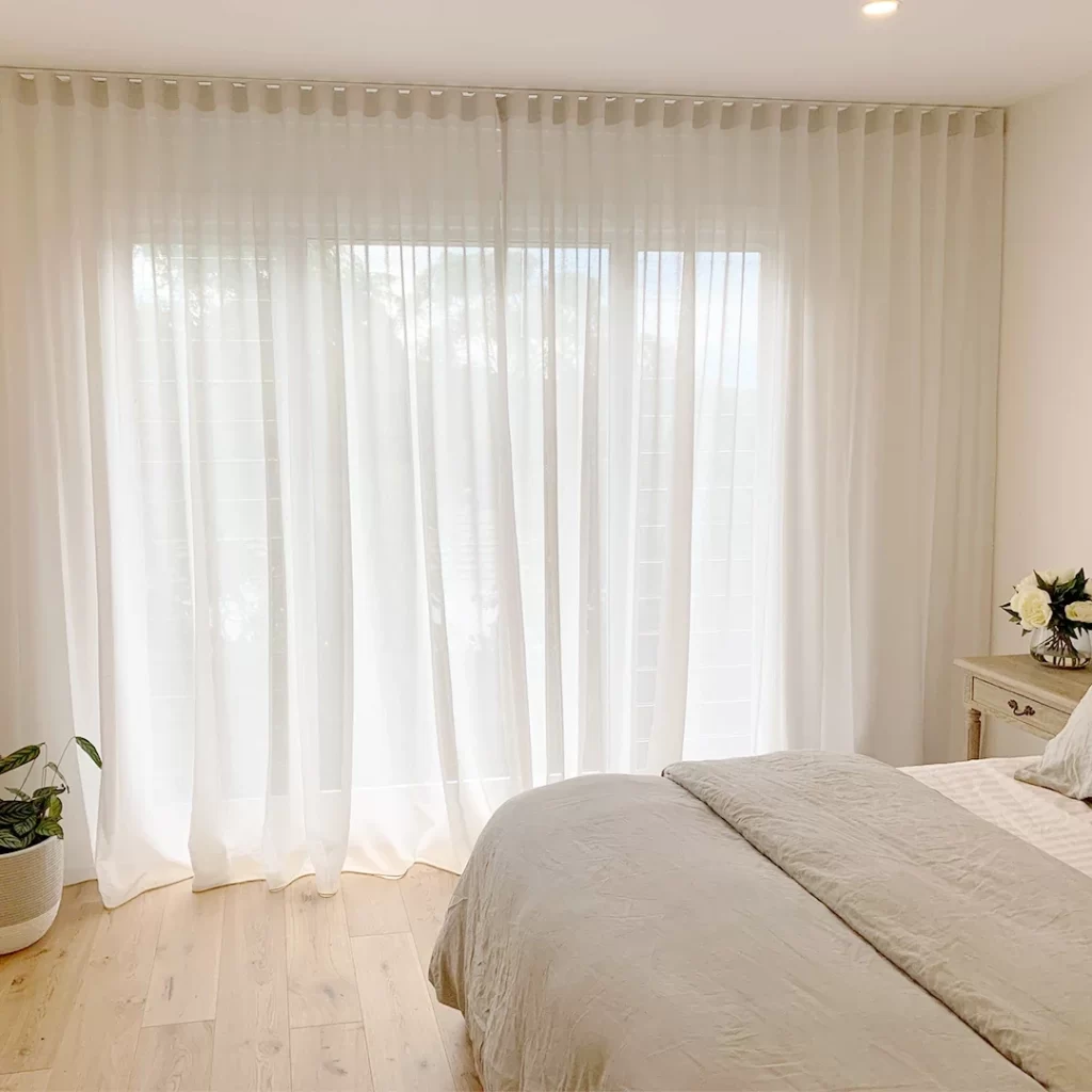 Bright bedroom with sheer white curtains over a large window