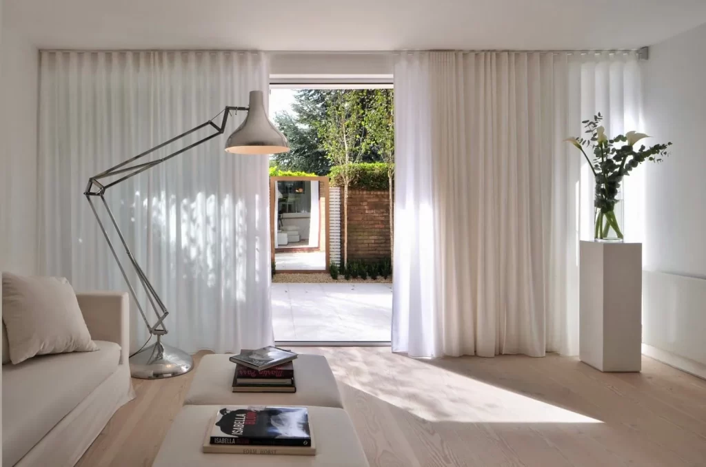 Modern living room with white curtains framing a sliding glass door to a garden