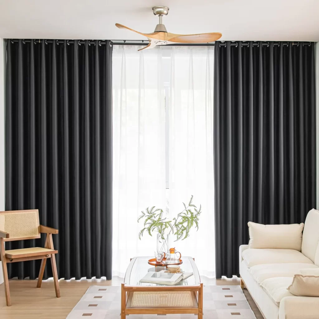 Modern living space with dark drapes, light furniture, and a wooden ceiling fan