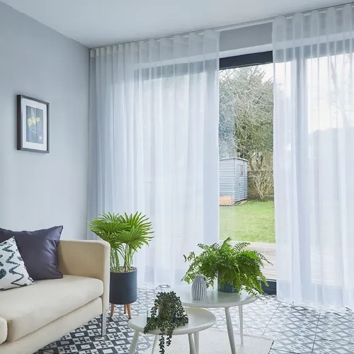 A pair of white sheer curtains with a delicate floral lace pattern is tied in the middle, creating a scalloped design.