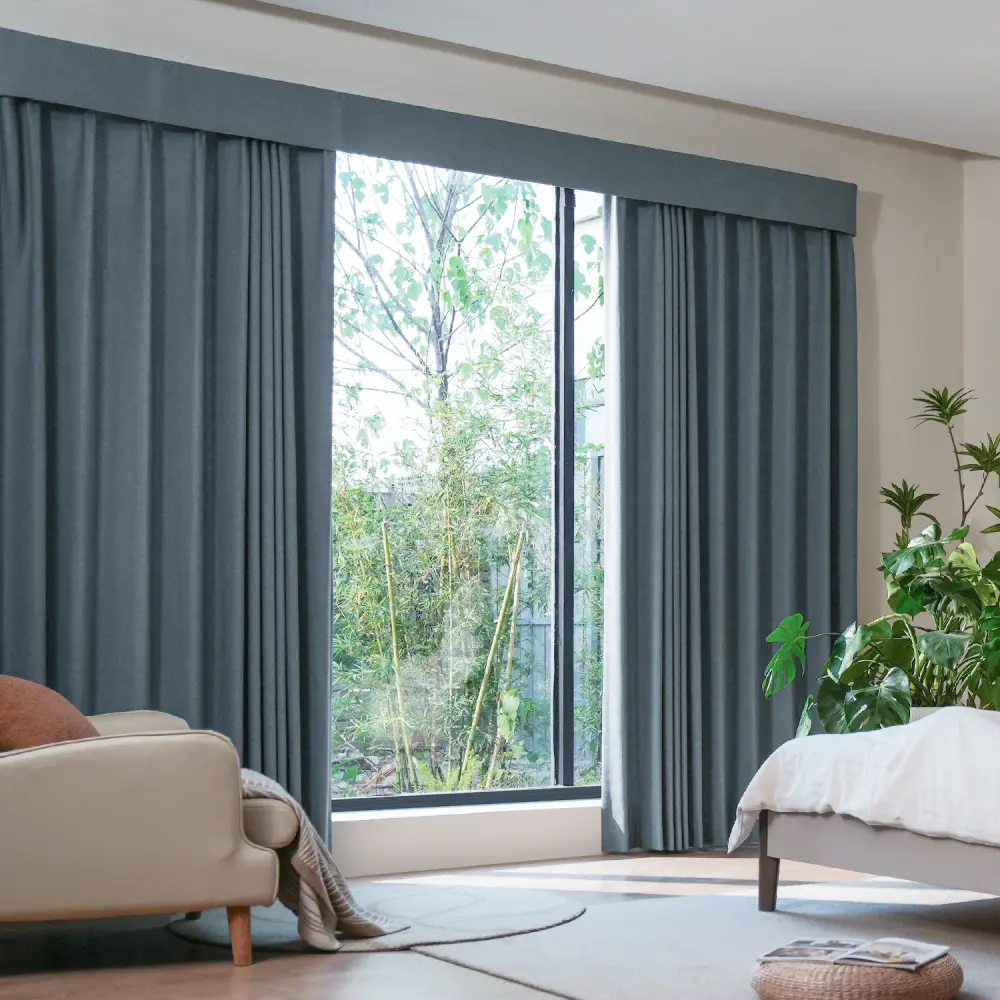 Bedroom window with floor-length blue-gray custom Blackout curtains Dubai and a view of trees.