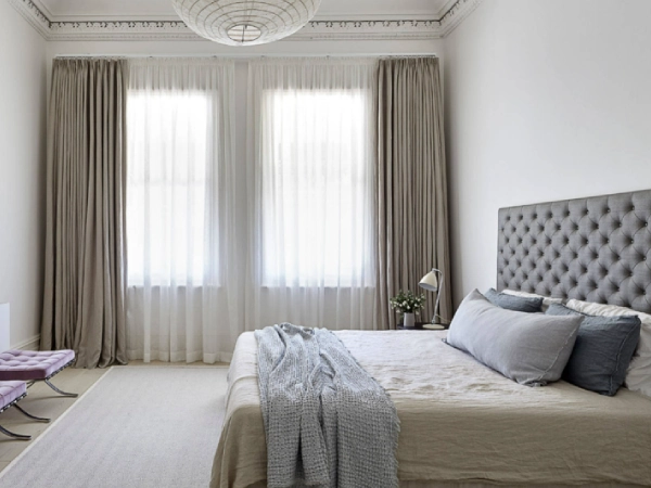 Bright, neutral bedroom with layered Blackout With Sheer Combo Dubai drapes and a tufted grey headboard.