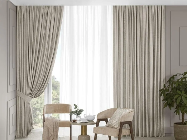 Elegant beige cotton blackout curtains in a Dubai living room with two chairs and a side table.