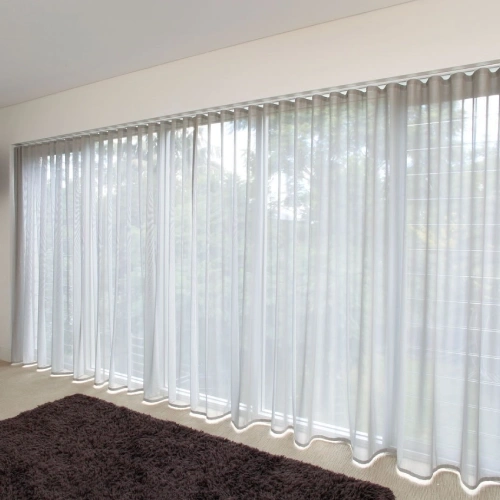 Wall of white floor-to-ceiling ripple fold sheer curtains over glass doors and a dark rug