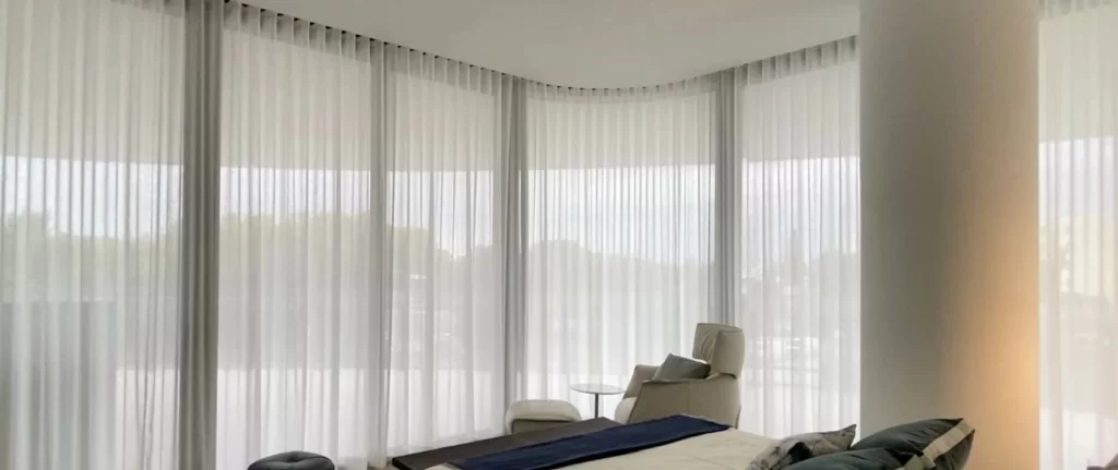 White sheer curtains draped across a large window, allowing soft, diffused sunlight to fill a modern, elegantly decorated room in Dubai.