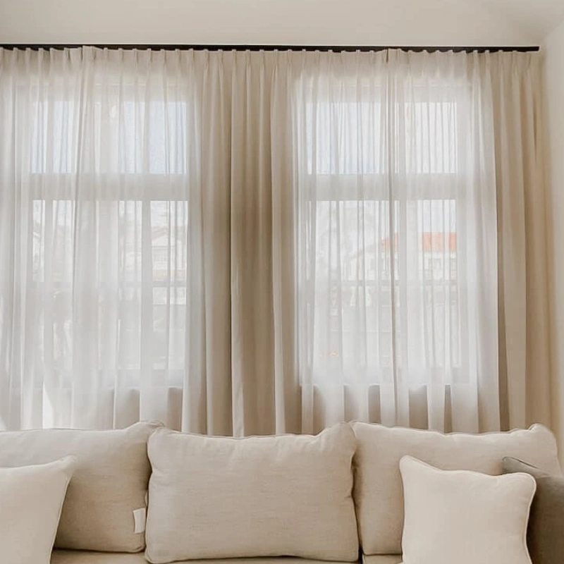 Hand holding a remote to operate motorized curtains in a luxury bedroom with a sea view.