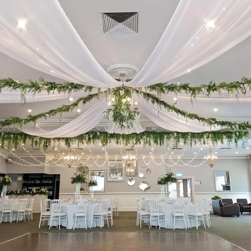 White ceiling drapes and fabric ceiling curtains with greenery for a romantic wedding decor.